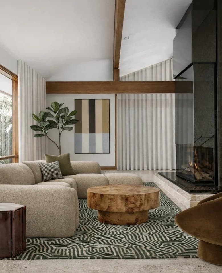 Mid-century living room with exposed timber beams, a painted brick fireplace wall, a bouclé modular sofa, a burl timber coffee table and a green patterned rug